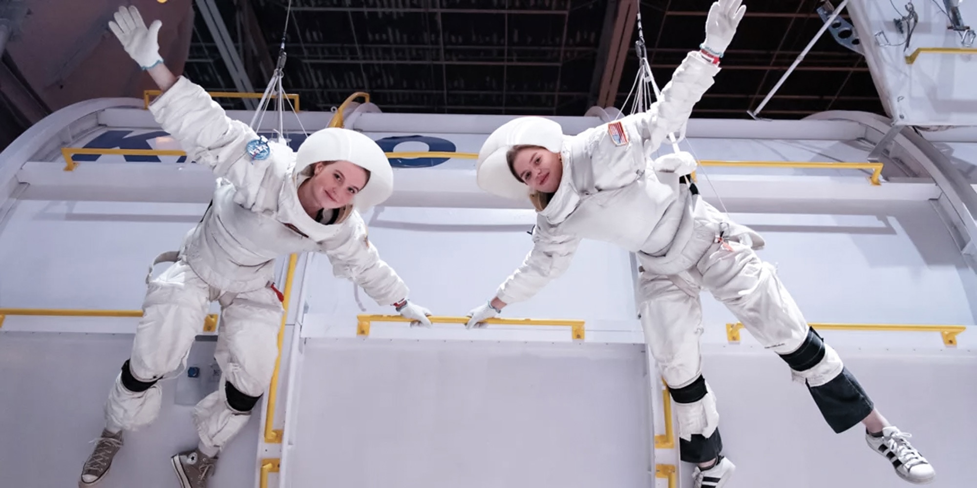 Two participants in astronaut suits suspended in training environment.