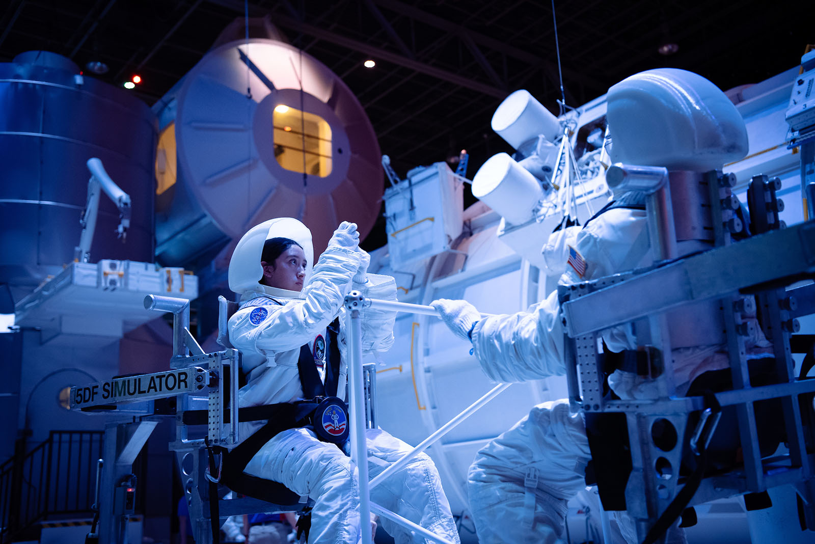 Students in astronaut suits practice maneuvers inside a space training simulator.