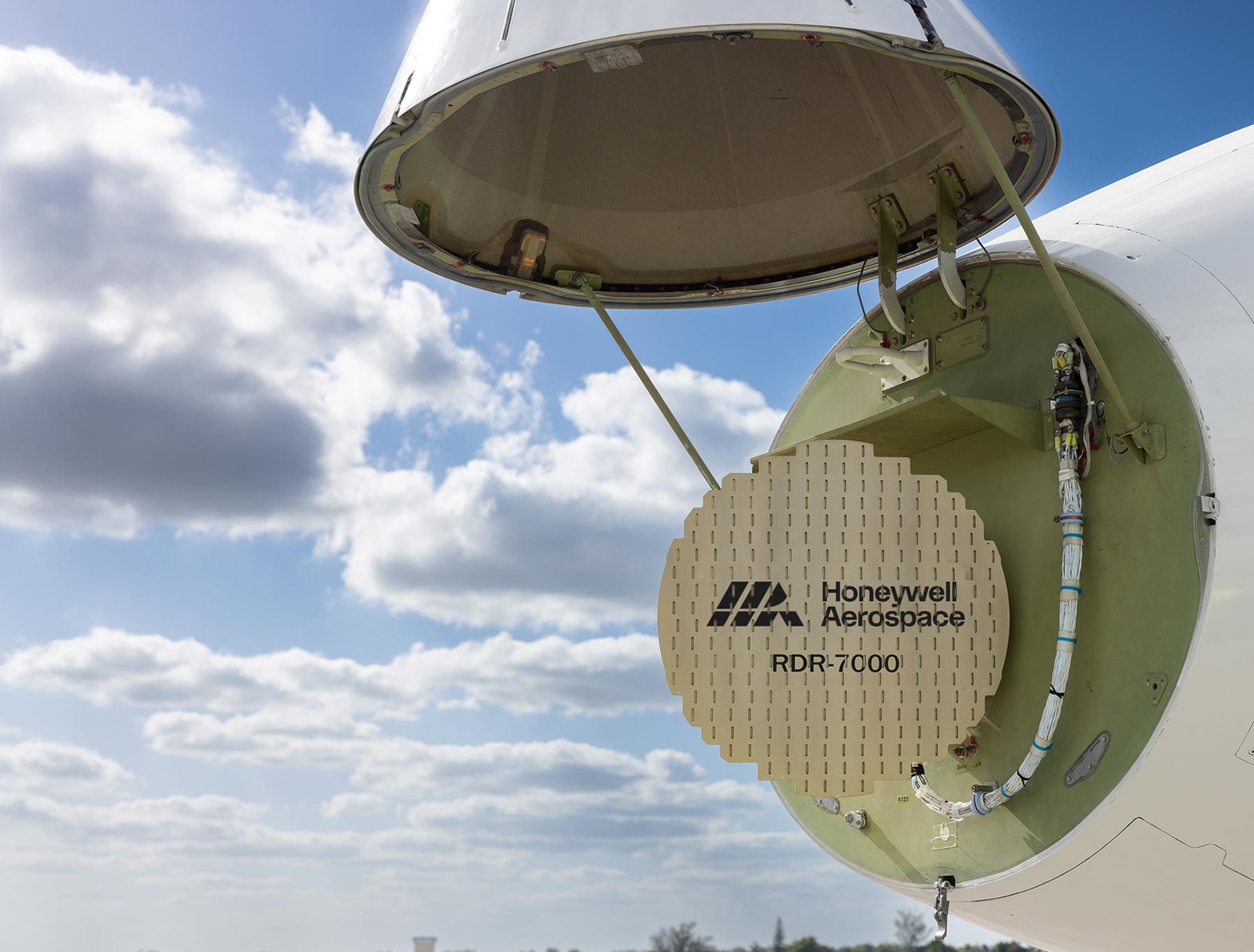 An aircraft’s nose compartment is open, revealing the Honeywell Aerospace RDR‑7000 radar system against a bright sky. The image highlights advanced radar technology and aircraft maintenance access.