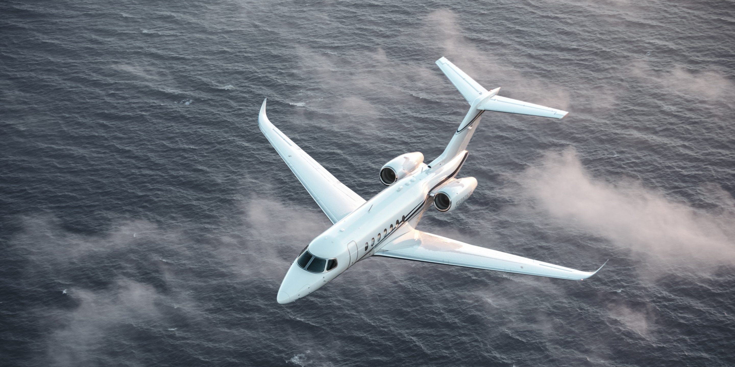 Cessna Longitude super midsize jet flying over water and clouds