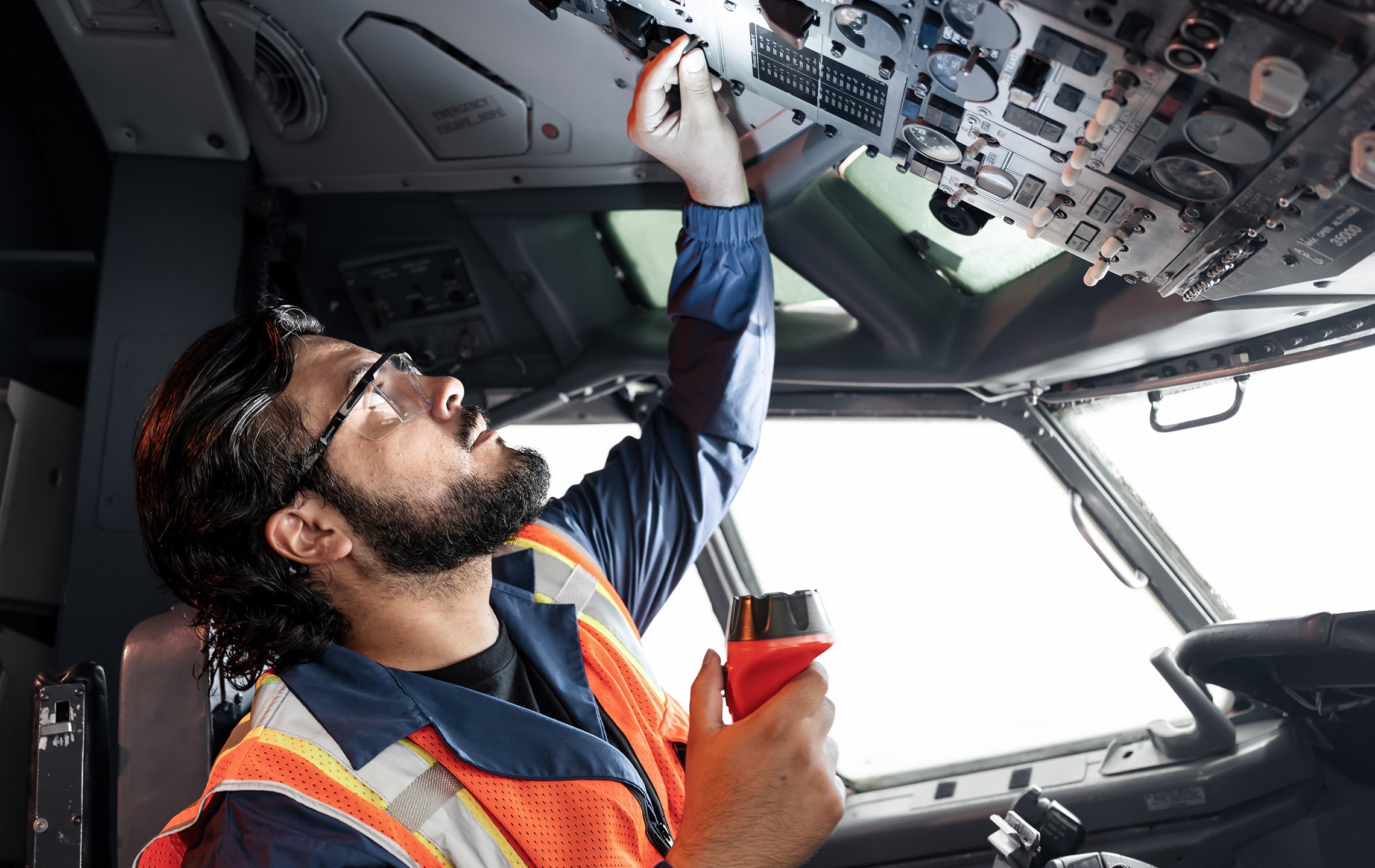 aviation maintenance technician performing checks on the overhead instrument panel inside an aircraft cockpit.