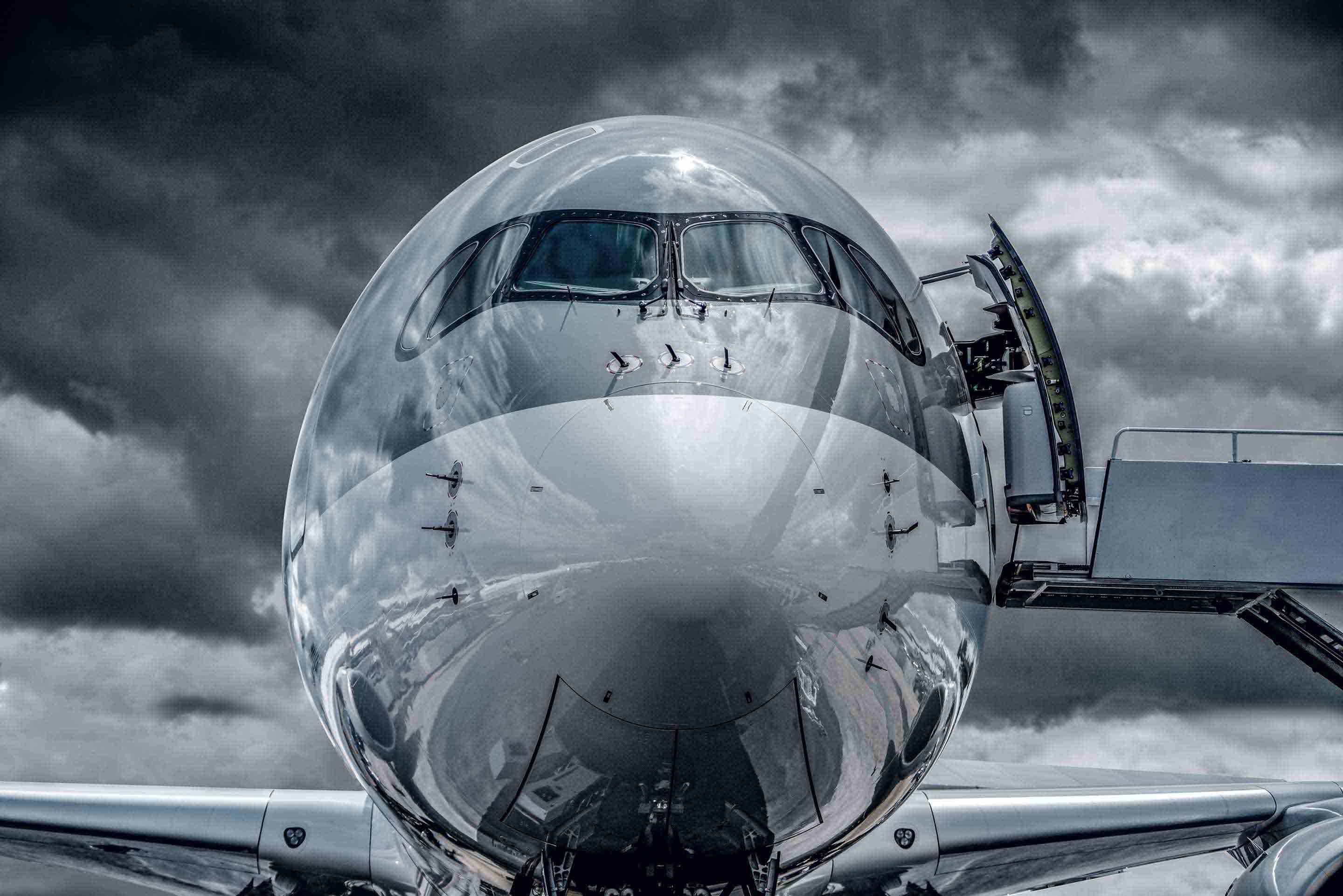 Head-on view of a large passenger aircraft on the tarmac with dark clouds creating a powerful, high-contrast atmosphere.