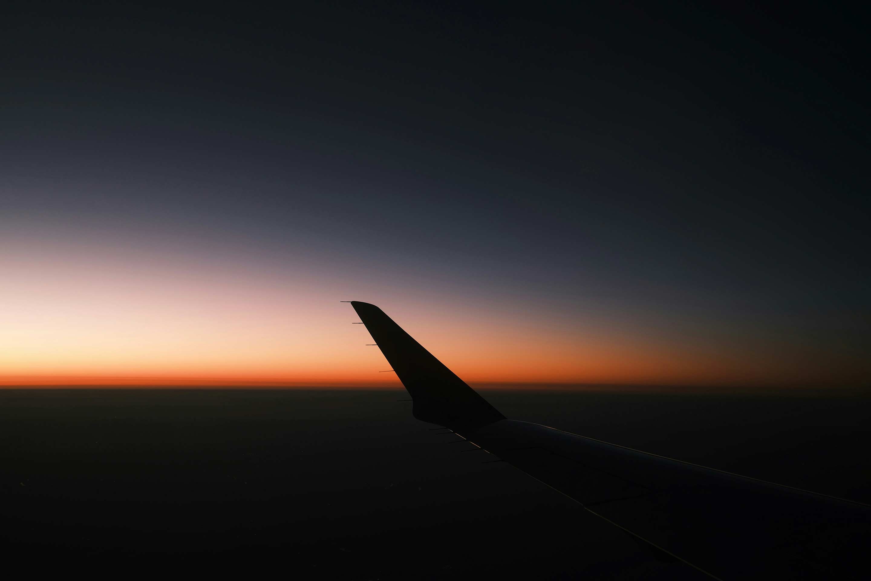 Passenger window view showing a wing silhouetted against a glowing sunset gradient.