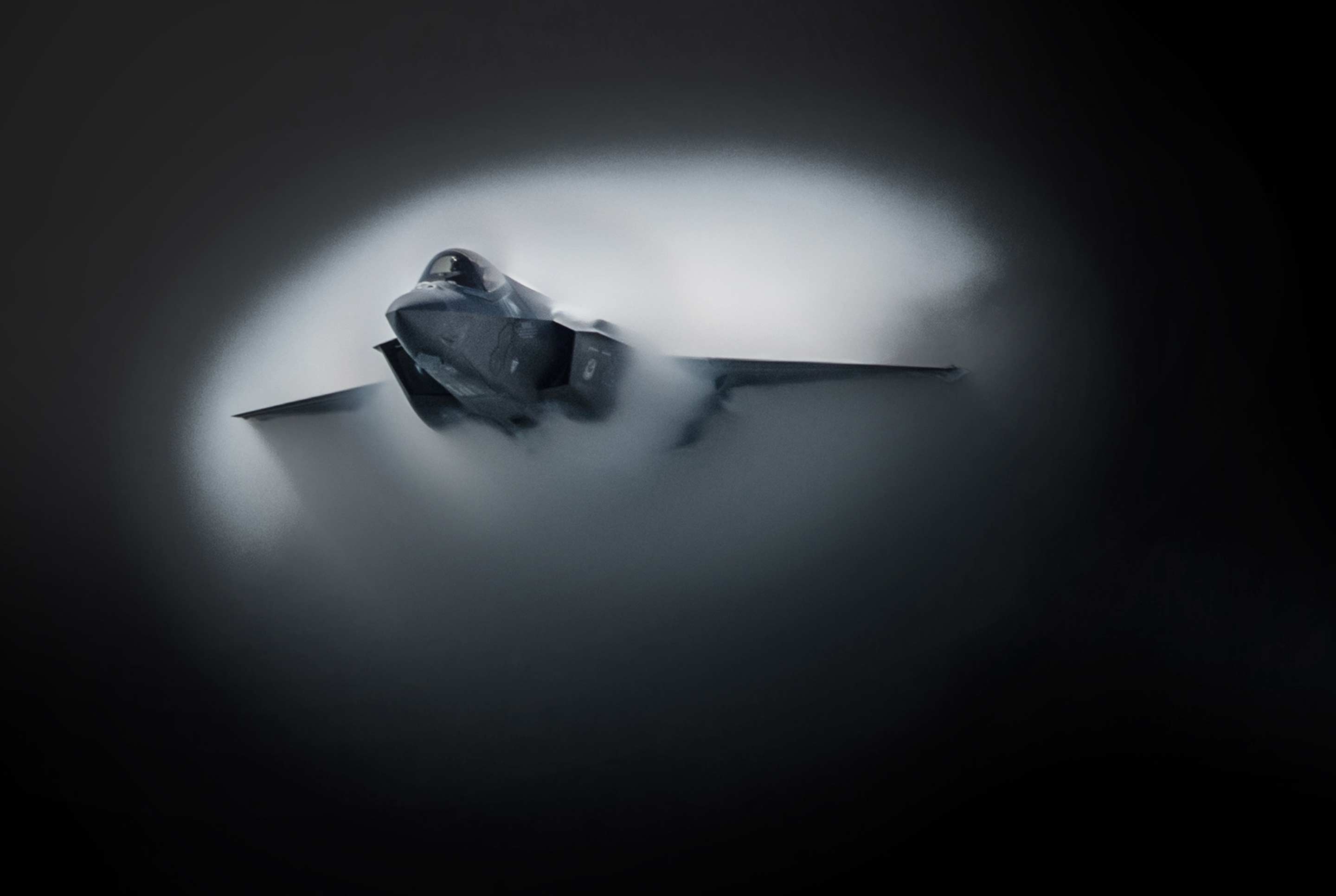 Advanced fighter aircraft cutting through condensed air, forming a circular vapor cloud during high-speed maneuvering.