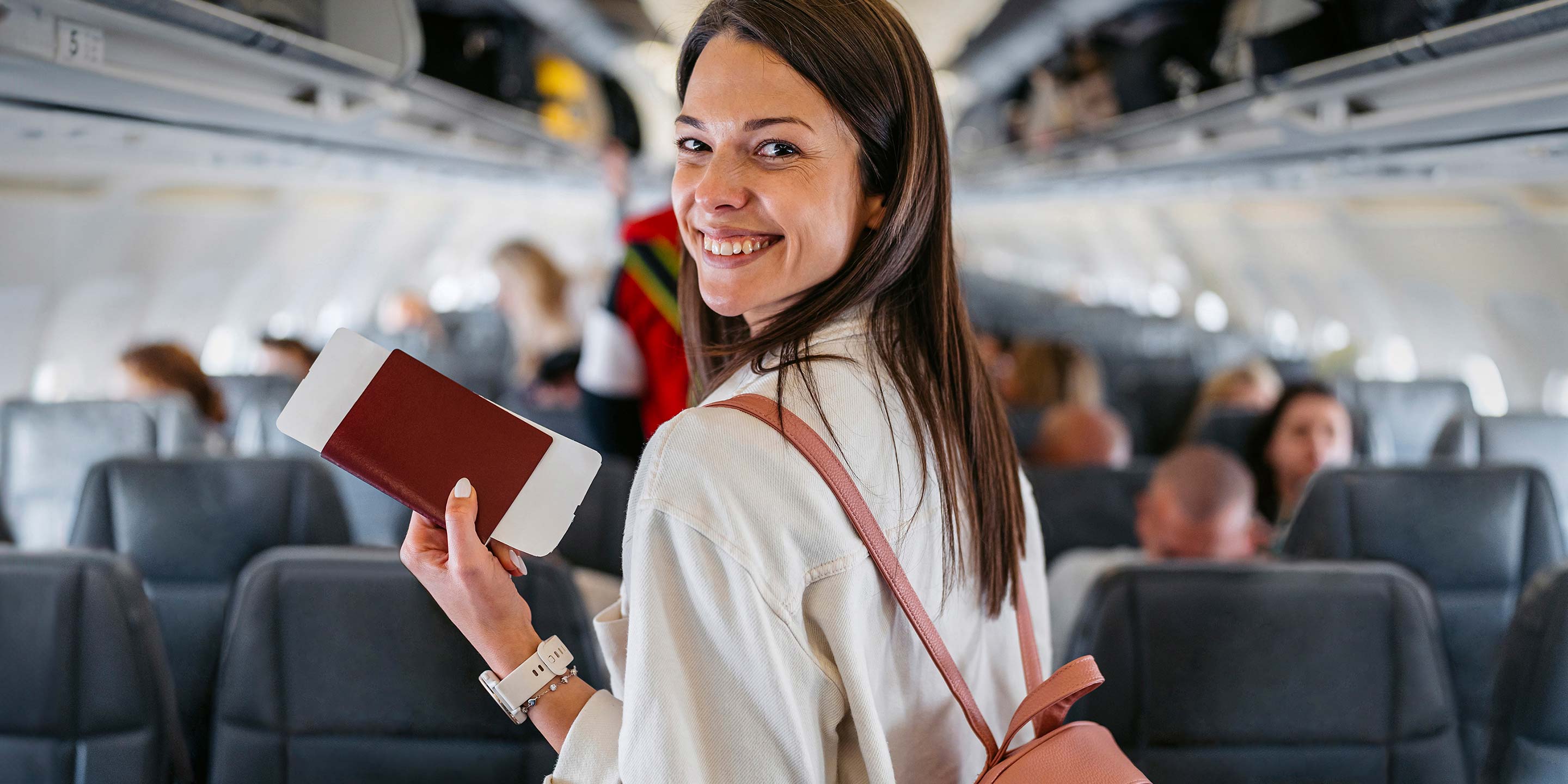 A woman holding her boarding pass and smiling at the camera inside the plane