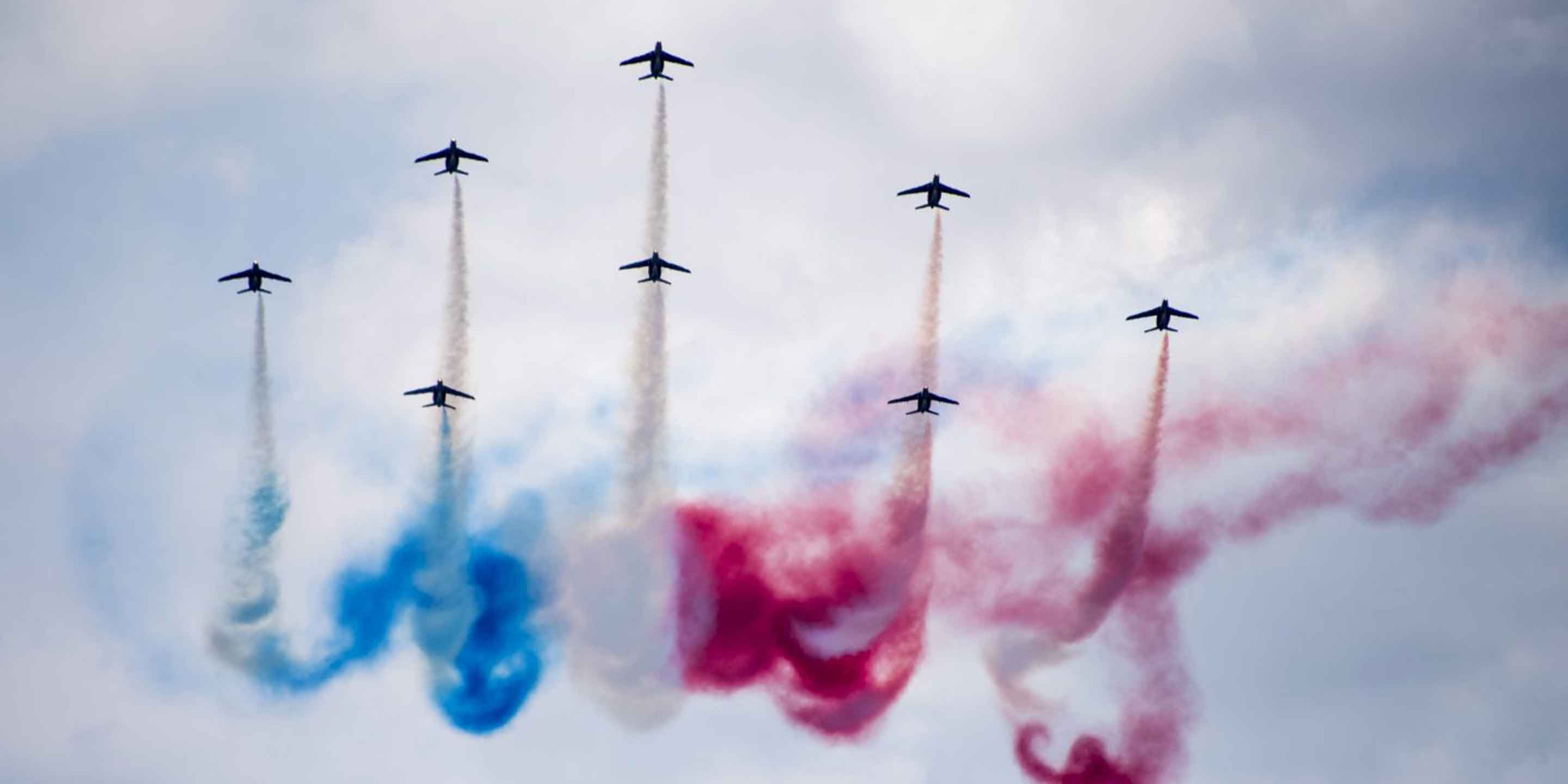 Several planes flying in formation, creating vibrant red, white, and blue smoke trails in the sky.