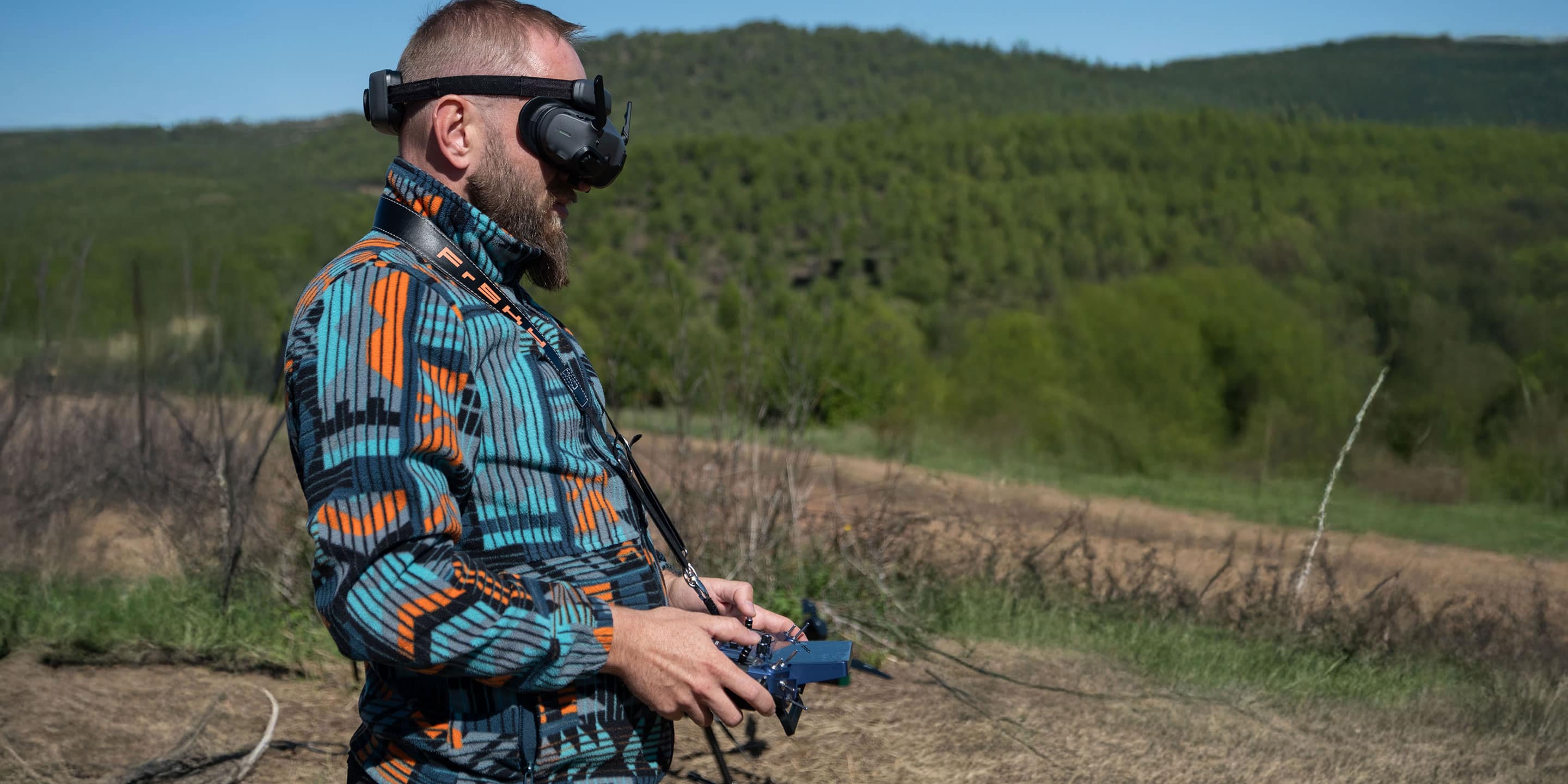 Operator controls HON Aero drone with FPV goggles and handheld transmitter during outdoor field testing in a natural environment.