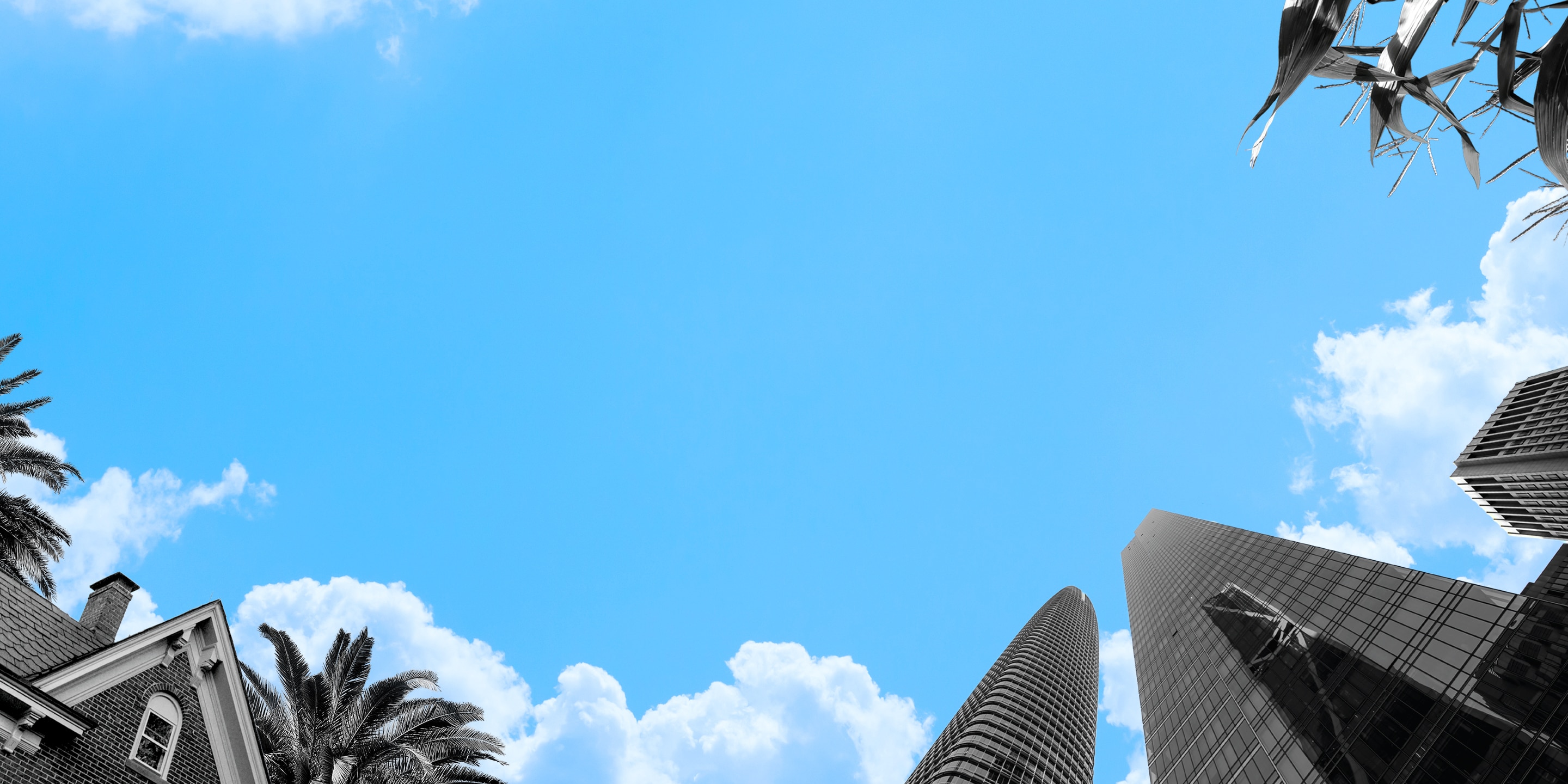 low-angle shot looking up at a blue sky framed by buildings and palm trees