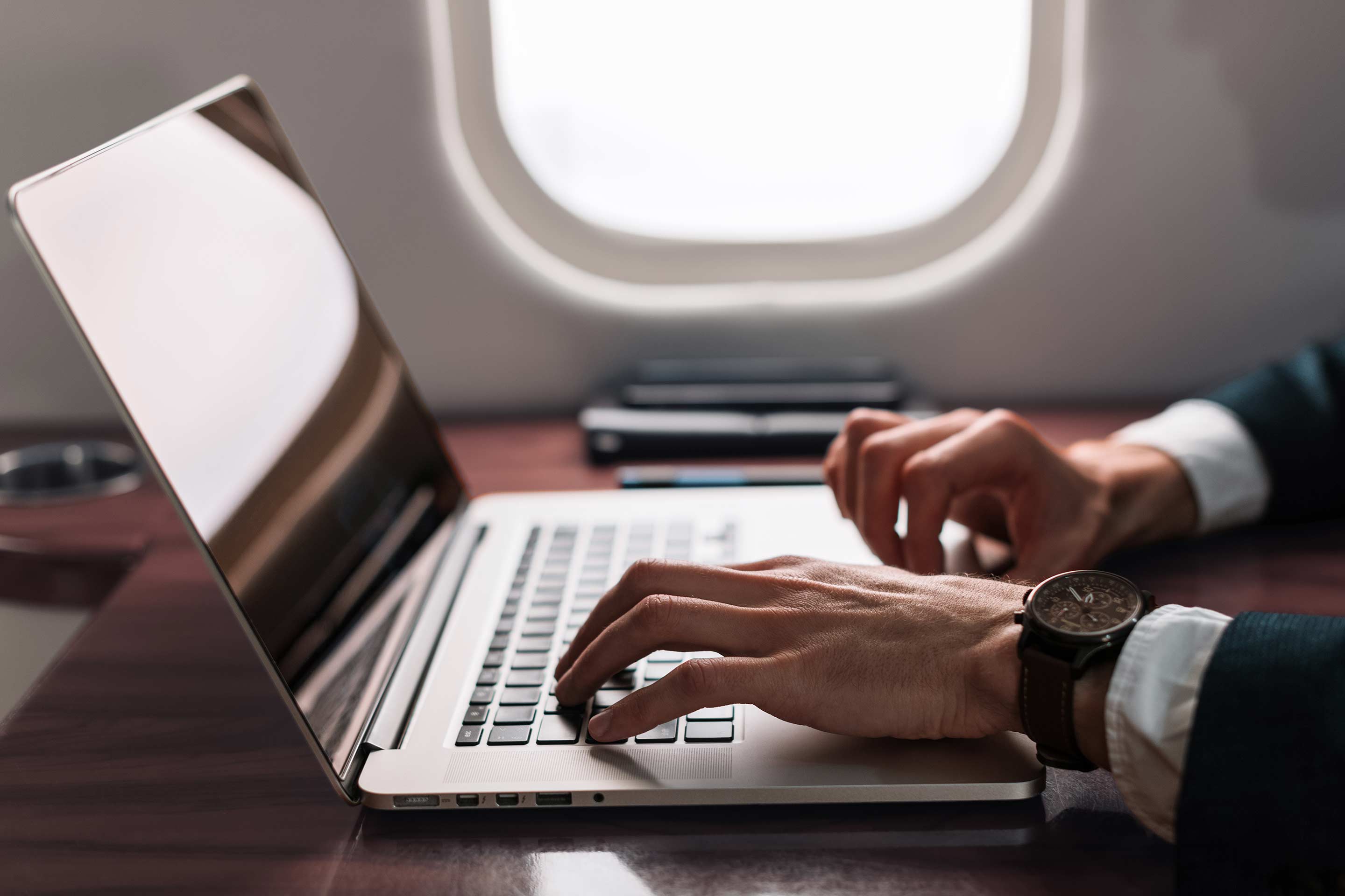 Hands working on laptop near airplane window
